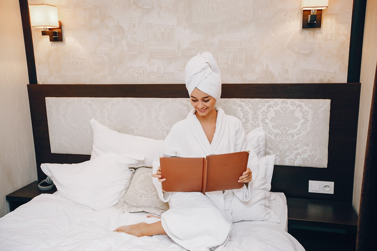 Mulher lendo livro com roupa de cama de hotel Mulher lendo livro com roupa de cama de hotel